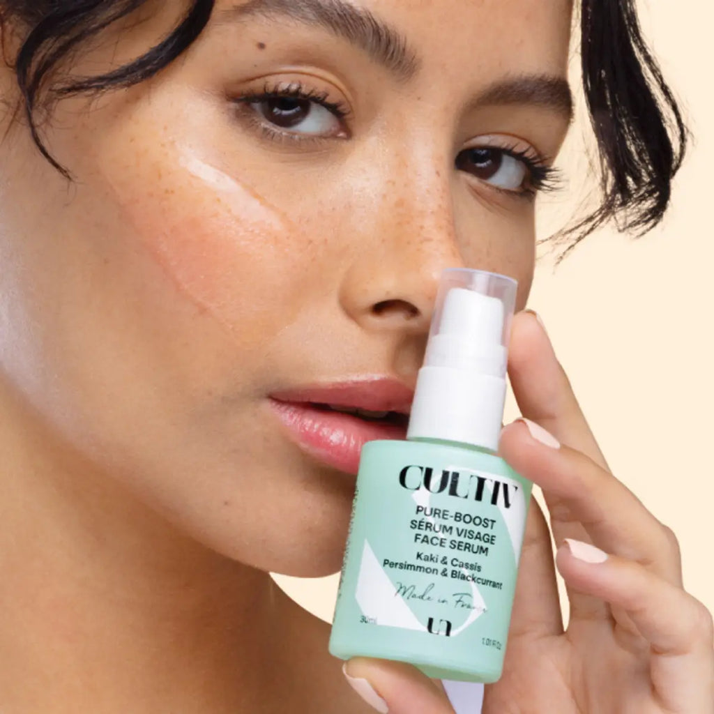 Woman holding a CULTIV skincare serum bottle close to her face on a beige background