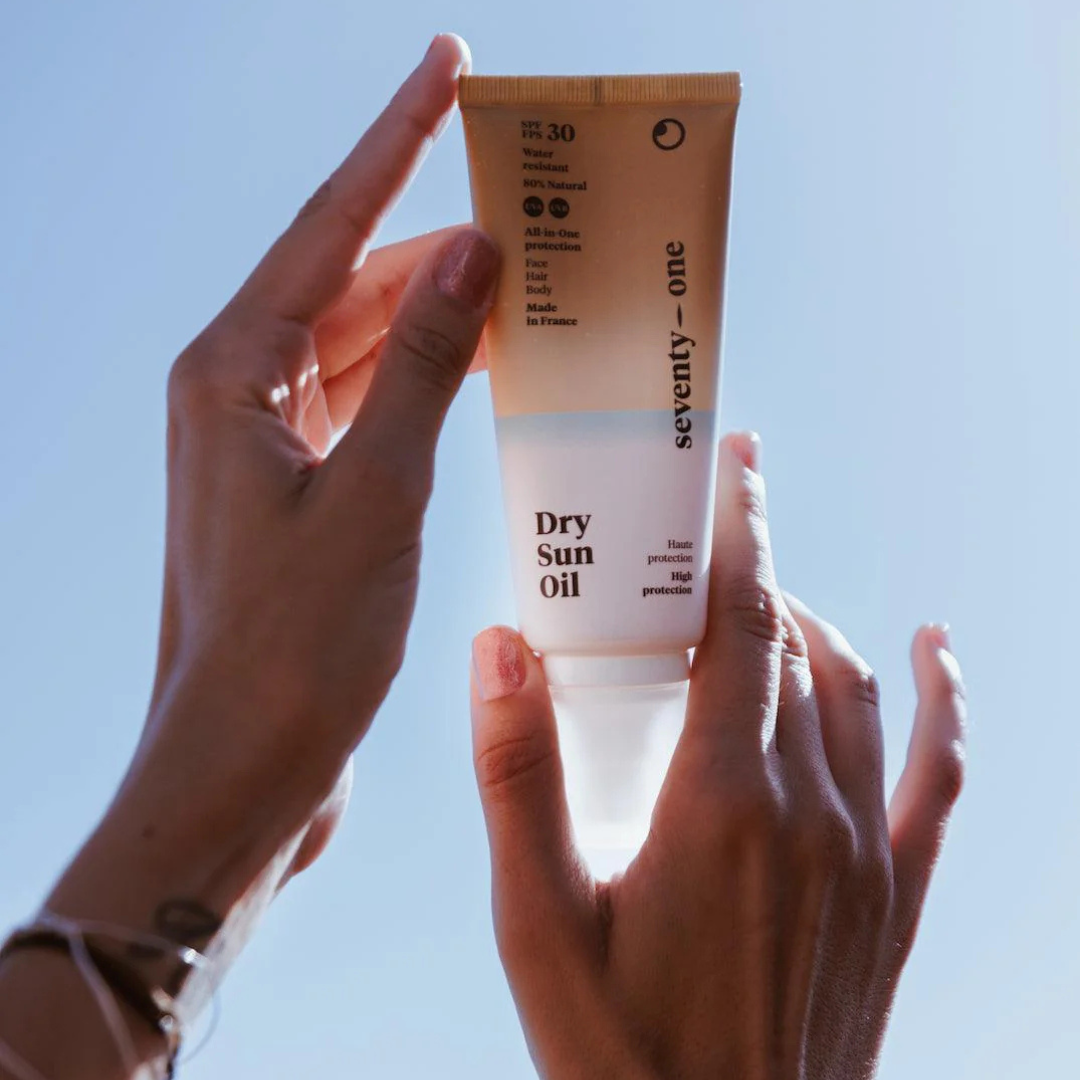 Hand holding a tube of 'seventy-one' Dry Sun Oil against a clear blue sky