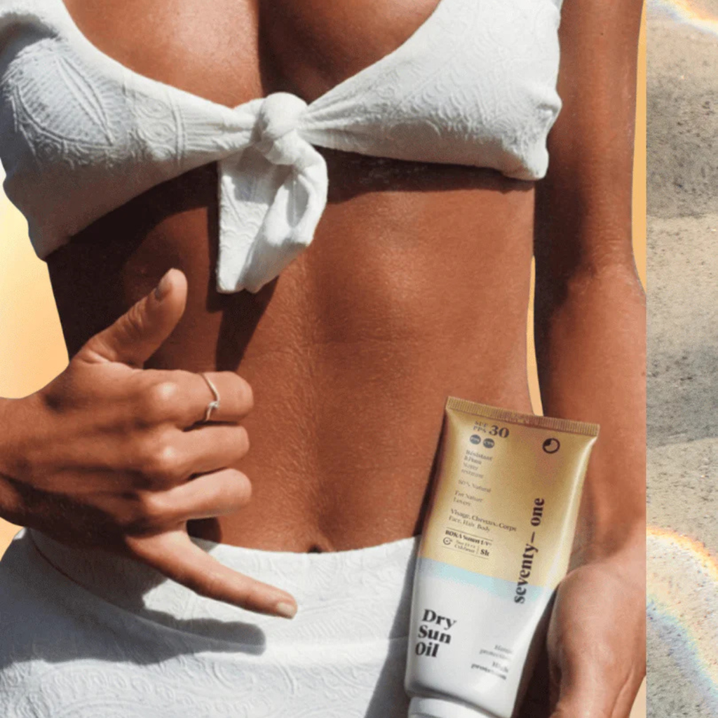 Person applying sunscreen with a tube of Seventy One Percent Dry Sun Oil on a beach setting.