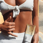 Person applying sunscreen with a tube of Seventy One Percent Dry Sun Oil on a beach setting.