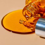 Close-up of a Oden Vitamine oil bottle pouring amber-colored liquid onto a beige surface.