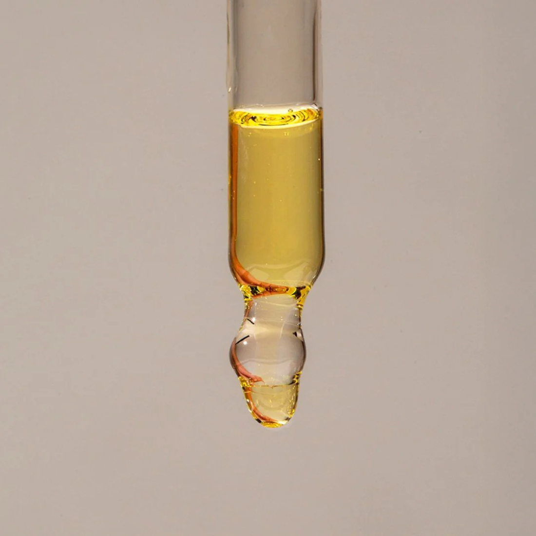 Glass dropper with yellow liquid on a gray background