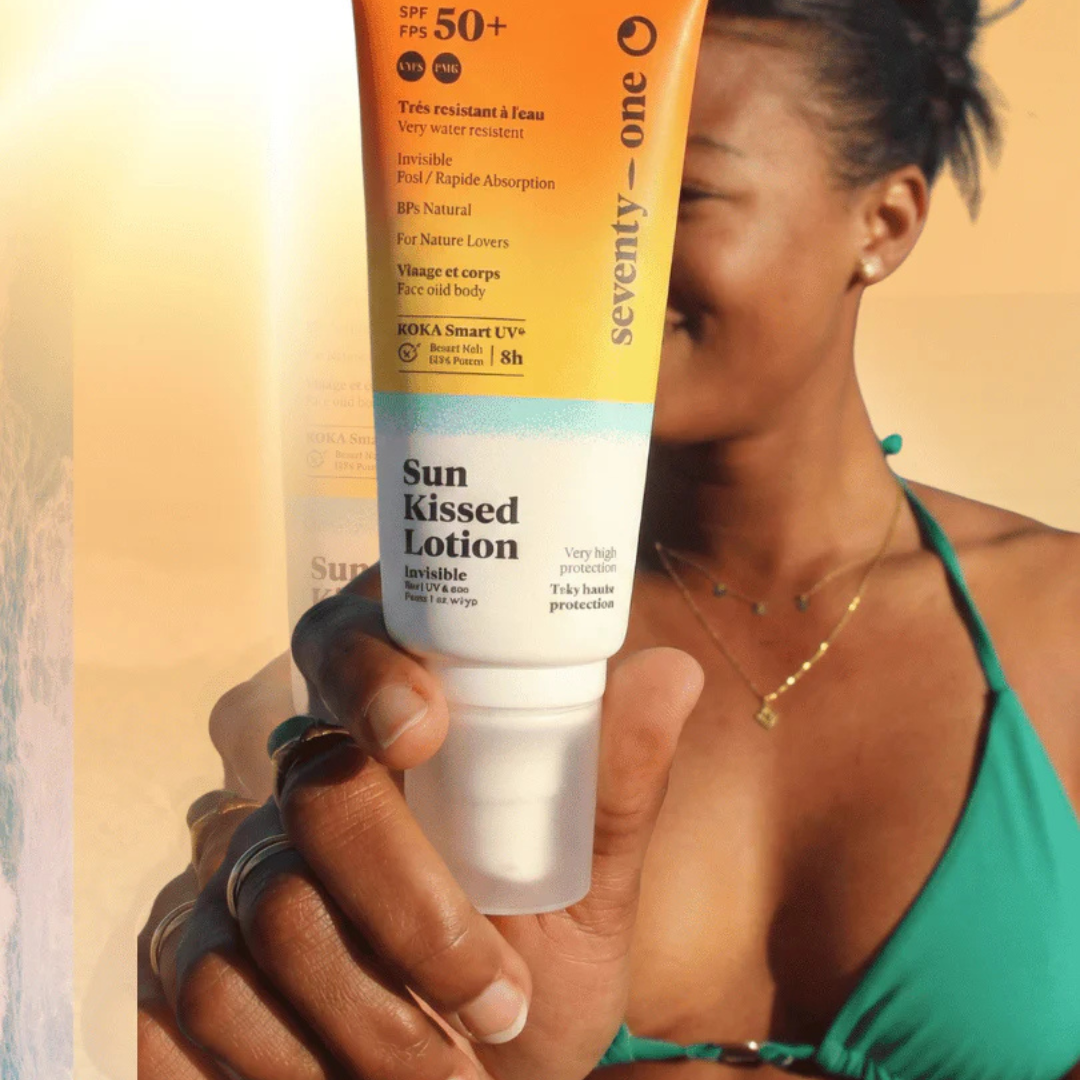 Person holding a tube of 'Seventy One Percent' Sun Kissed Lotion with SPF 50+ against a warm background.