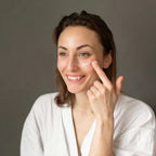 Woman applying cream to her face against a neutral background