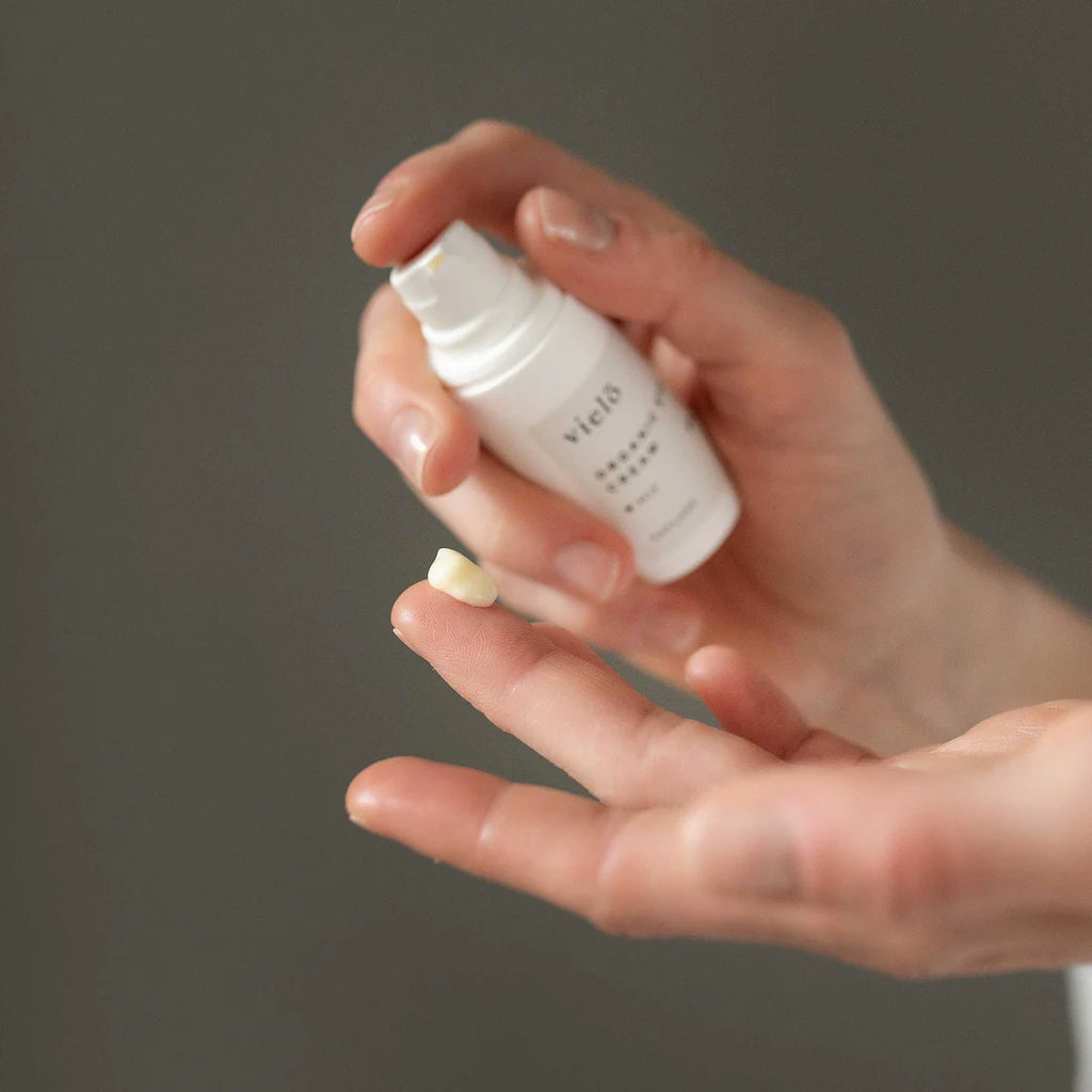 Hand holding a Vielö Organic eye cream bottle against a dark background