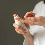 Person holding a white spray bottle with a brand name on a neutral background