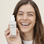 Woman holding a ODEN skincare product against a neutral background